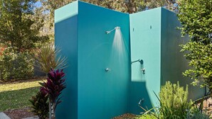 Een buiteninrichting met een douchecabine in groenblauw, voorzien van een handdouche, omringd door verschillende planten.