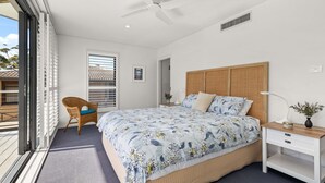 Een slaapkamer met een groot bed, een stoel, een bureau en een plafondventilator.