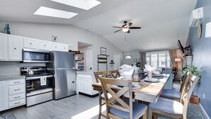 Une cuisine moderne avec des meubles blancs, un réfrigérateur en acier inoxydable et un coin repas comprenant des chaises et une table en bois.