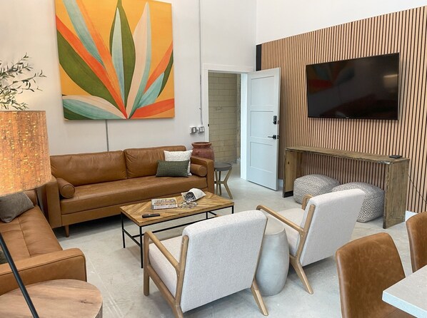 Una sala de estar moderna con un sofá de cuero marrón, una mesa de centro de madera y un televisor montado en una pared de madera.