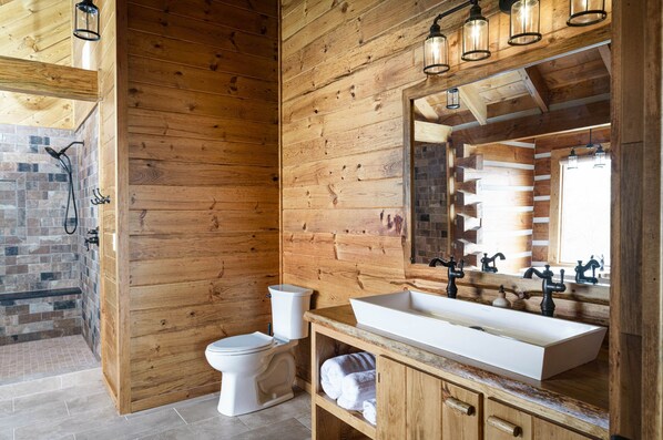 A wooden-paneled bathroom with a large mirror, a white sink, and a toilet. - Cliffside Romantic Retreat LOVE (Pine Ridge)
