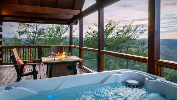 Een hottub op een houten terras met uitzicht op bomen en bergen.
