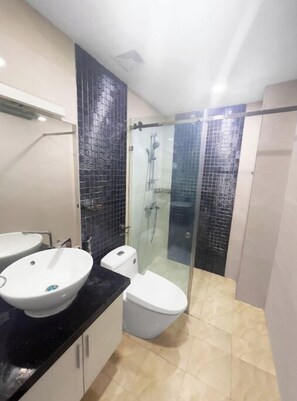 Modern bathroom with two pedestal sinks, a toilet, and a shower area with a clear glass door.