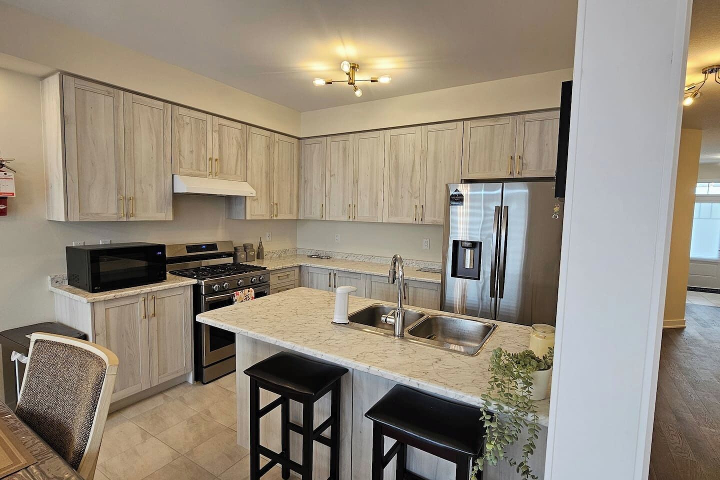 A modern kitchen with light wood cabinets, a stainless steel refrigerator, a microwave, and a gas stove.