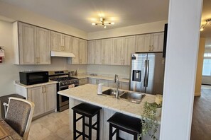 Une cuisine moderne avec des meubles de couleur bois clair, un réfrigérateur en acier inoxydable, un four à micro-ondes et une cuisinière à gaz.