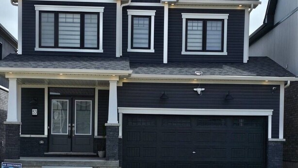 A two-story house with a dark exterior, a garage, and a front porch. - Beautiful Home backing on Welland Canals STR-289 (Welland)