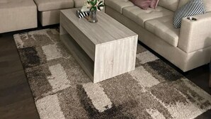 A modern living room with a sectional sofa, a coffee table, and a large window with blinds. - Beautiful Home backing on Welland Canals STR-289 (Welland)