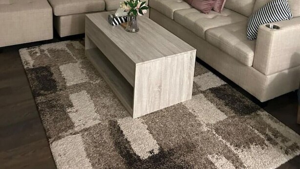 A modern living room with a sectional sofa, a coffee table, and a large window with blinds. - Beautiful Home backing on Welland Canals STR-289 (Welland)