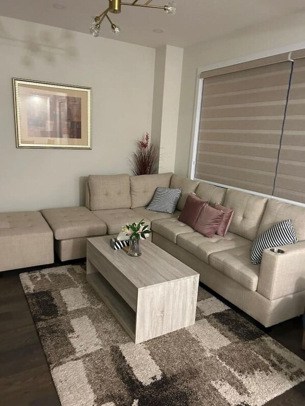 Una sala de estar moderna con un sofá seccional, una mesa de centro y un ventanal con persianas.