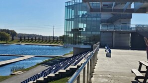 A modern building with a glass facade overlooking a river, a concrete deck with benches, and a clear sky. - Beautiful Home backing on Welland Canals STR-289 (Welland)