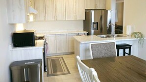 A modern kitchen with light wood cabinets, a stainless steel refrigerator, a microwave, and a dining area with a table and chairs. - Beautiful Home backing on Welland Canals STR-289 (Welland)