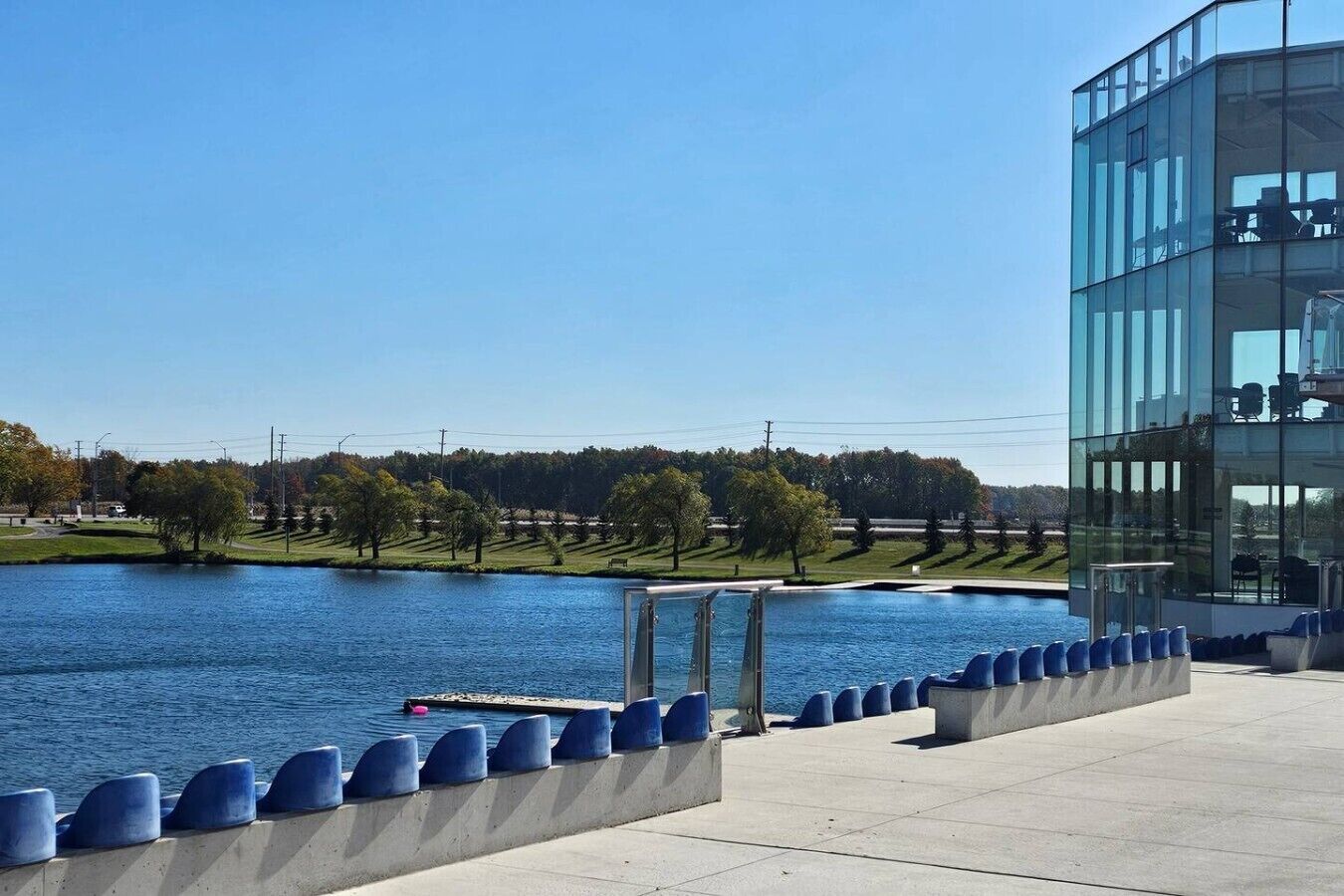 Un edificio moderno con fachada de vidrio que da a una masa de agua tranquila, un cielo despejado y un parque bien cuidado.