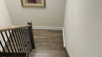 A wooden staircase with a metal railing, leading to a room with a framed abstract painting on the wall.