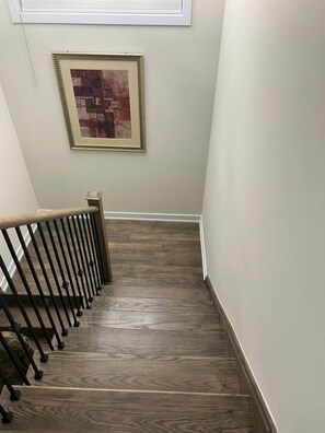 A wooden staircase with a metal railing, leading to a room with a framed abstract painting on the wall.