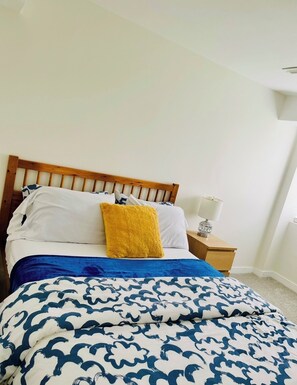 A bed with a wooden headboard, a patterned bedspread, a yellow pillow, and a bedside table with a lamp. - New, Clean and Comfortable Apartment with Private Entrance. (East Gwillimbury)