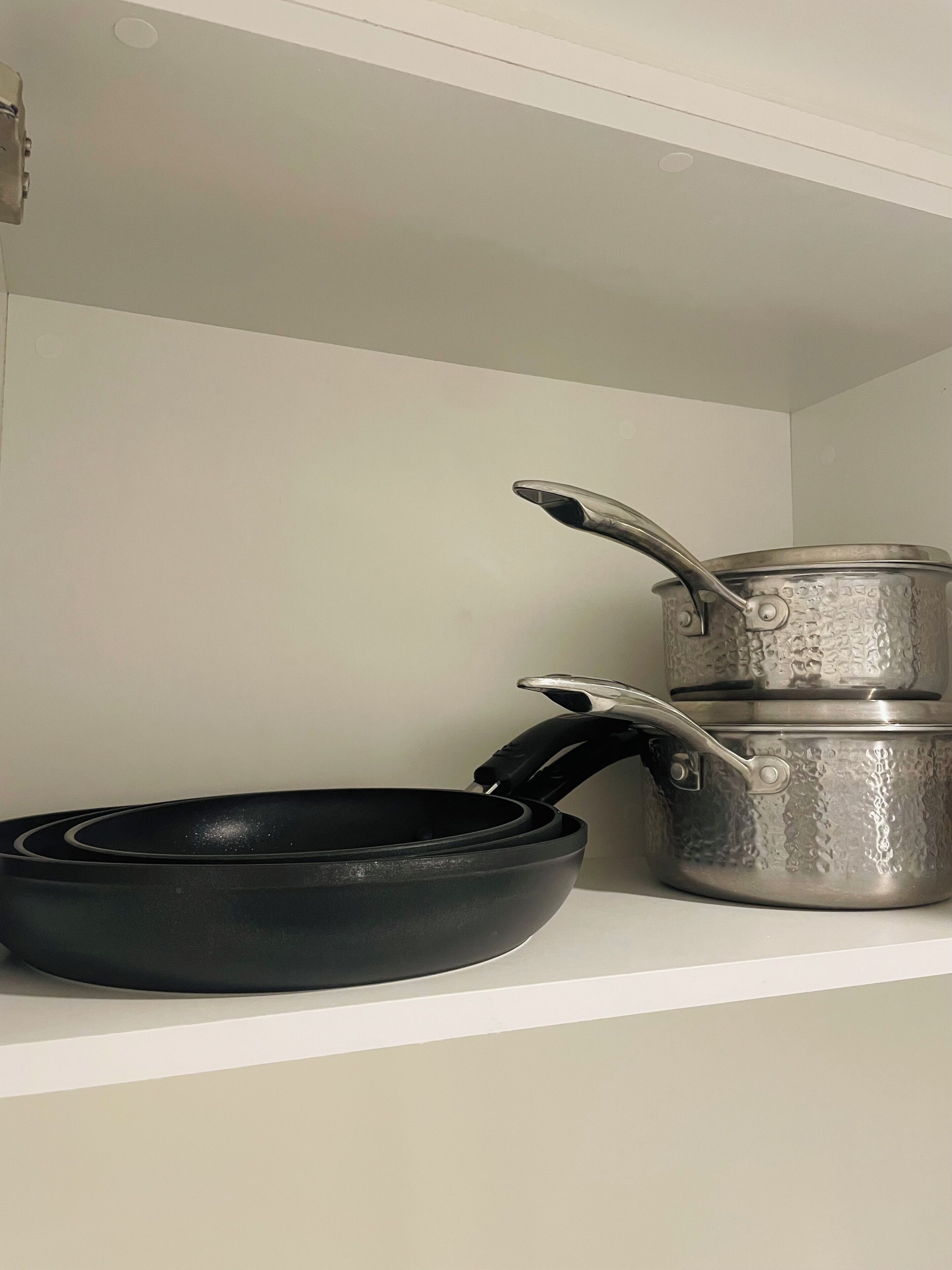 Une étagère de cuisine avec une poêle noire et deux casseroles en métal empilées.