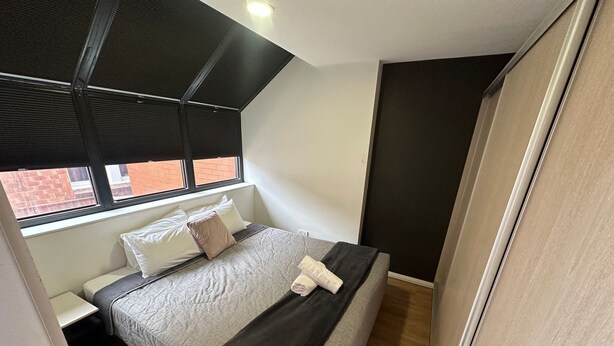 A bedroom with a bed, a window, a nightstand, and a wardrobe. - One Bedroom Apartment (Hamilton)