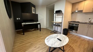 A compact kitchen with a microwave, stove, and sink. There's a small round table with a remote control on it. - One Bedroom Apartment (Hamilton)