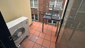 A small balcony with a tiled floor, a metal railing, and a large air conditioning unit. - One Bedroom Apartment (Hamilton)