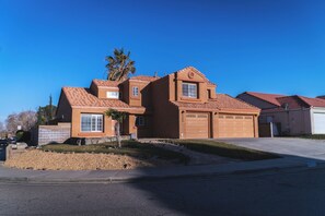 Une maison à deux étages avec un garage, un petit jardin devant et un palmier.