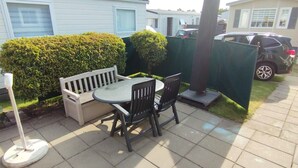 Un espace patio avec une table et des chaises, un banc blanc et une clôture verte.