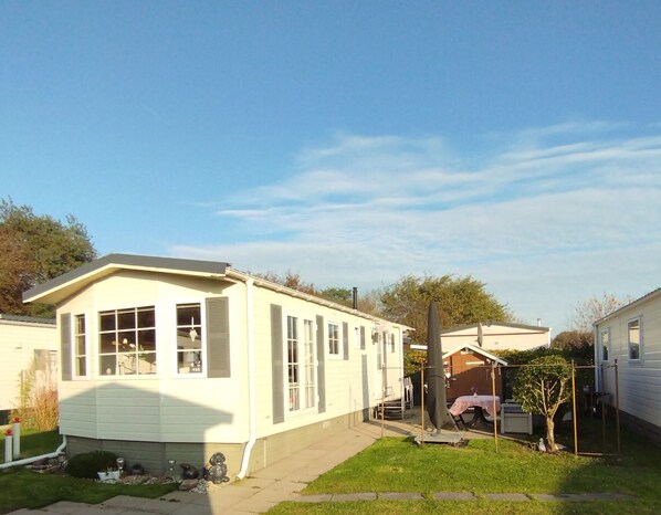 Ein eingeschossiges Mobilheim mit Veranda und kleinem Garten.