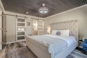 Ein Schlafzimmer mit einem großen Bett, einem gepolsterten Kopfteil, einem Kleiderschrank mit Milchglasschränken und einem Deckenventilator.