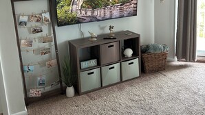 Ein Wohnzimmer mit Flachbildfernseher an der Wand, einem Holzunterhaltungsmöbel darunter, einem dekorativen Kranz und einer wandbefeusterten Pflanze.