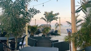 Ein Außenbereich mit Tischen und Stühlen, umgeben von Palmen, mit Blick auf einen Strand.
