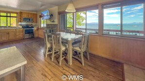Una cocina con armarios de madera, estufa y comedor con mesa y sillas. Hay un ventanal con vista al mar.