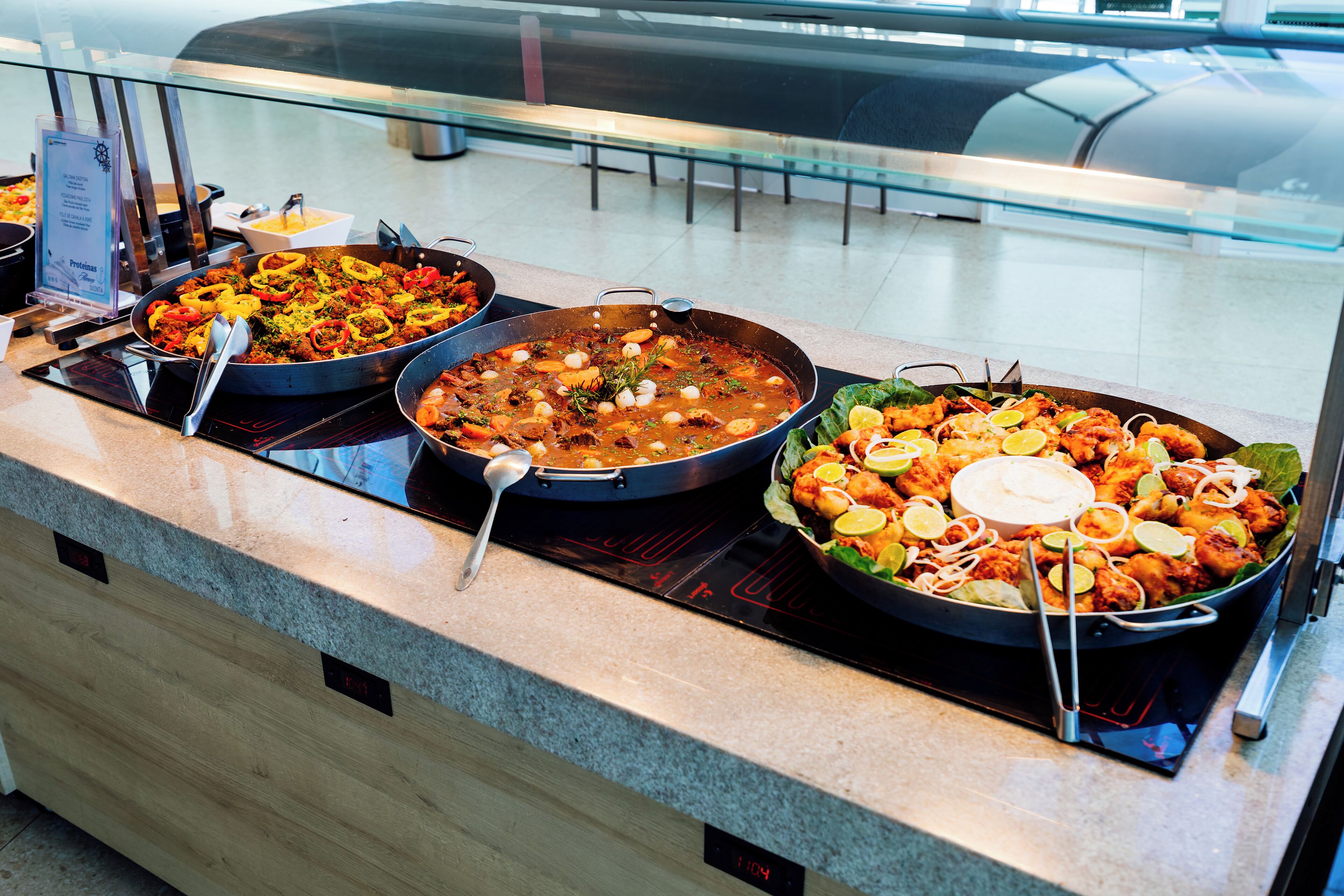 A buffet with various dishes, including seafood and salads, displayed on a counter with a digital clock.