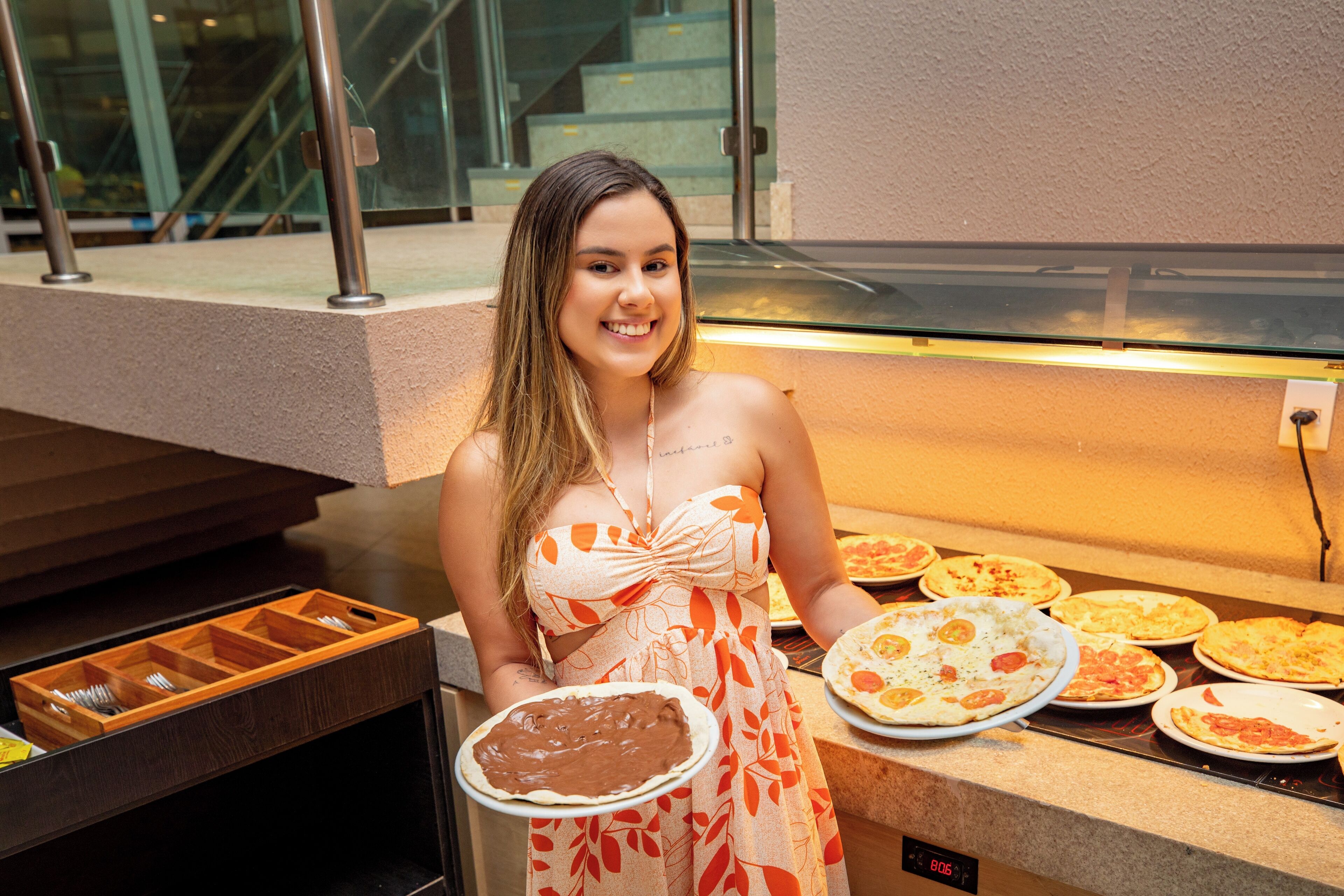 Un buffet proposant différentes sortes de pizzas, et une personne tenant une assiette avec un dessert au chocolat.