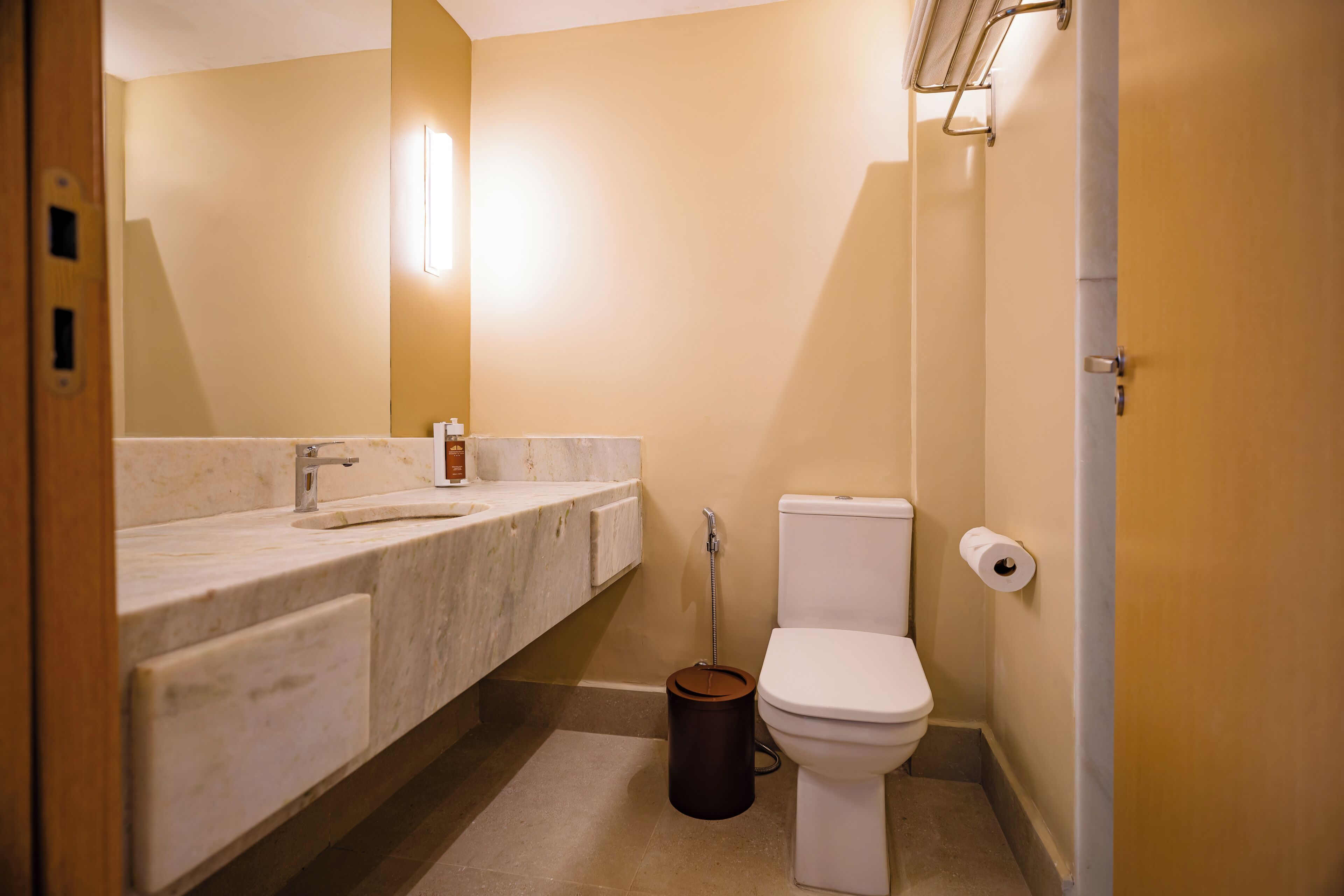 Un baño con lavamanos de mármol, un inodoro y un cubo de basura.