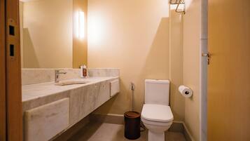 Un baño con lavamanos de mármol, un inodoro y un cubo de basura.