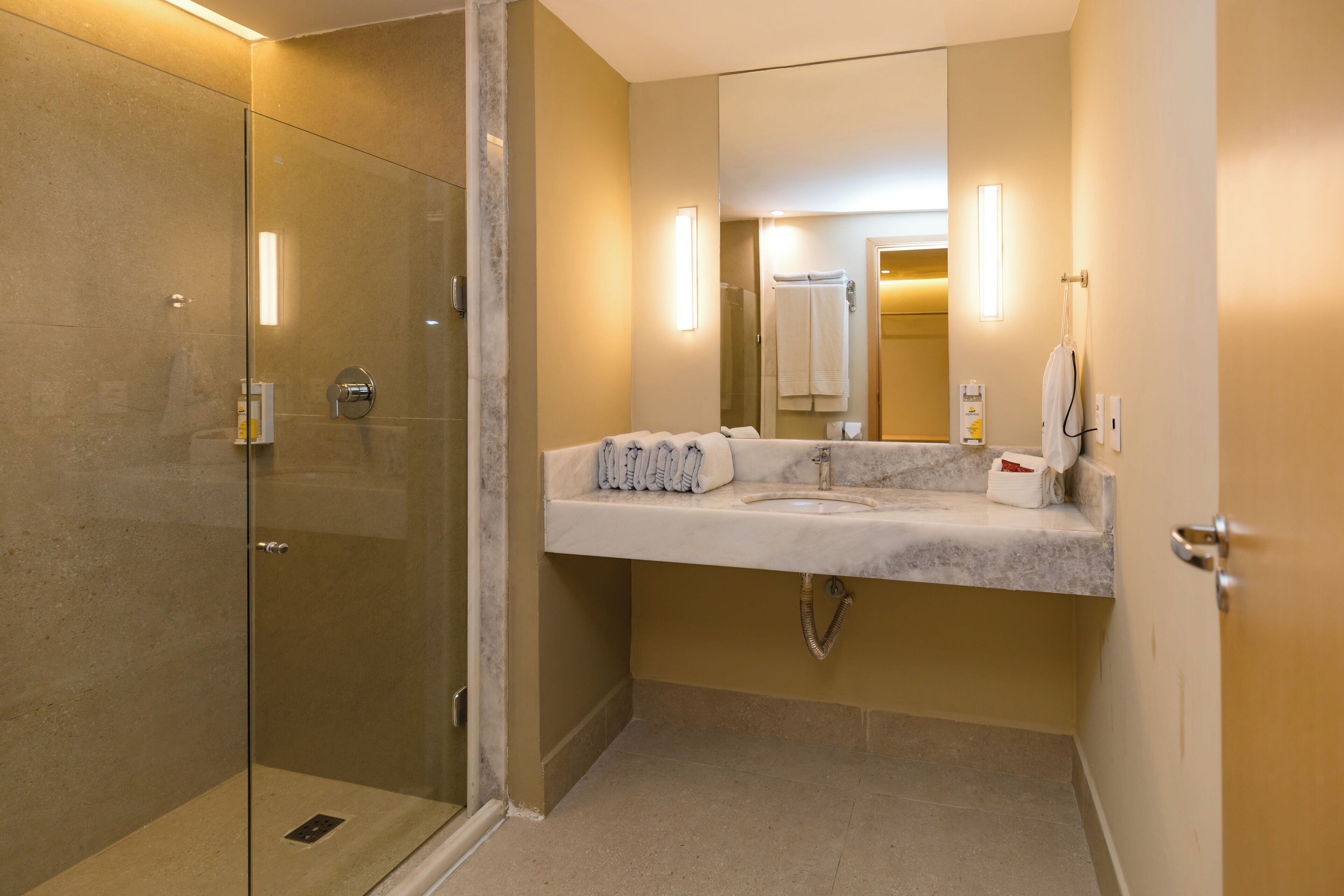 Un baño con cabina de ducha de vidrio, lavabo de mármol y un espejo grande.
