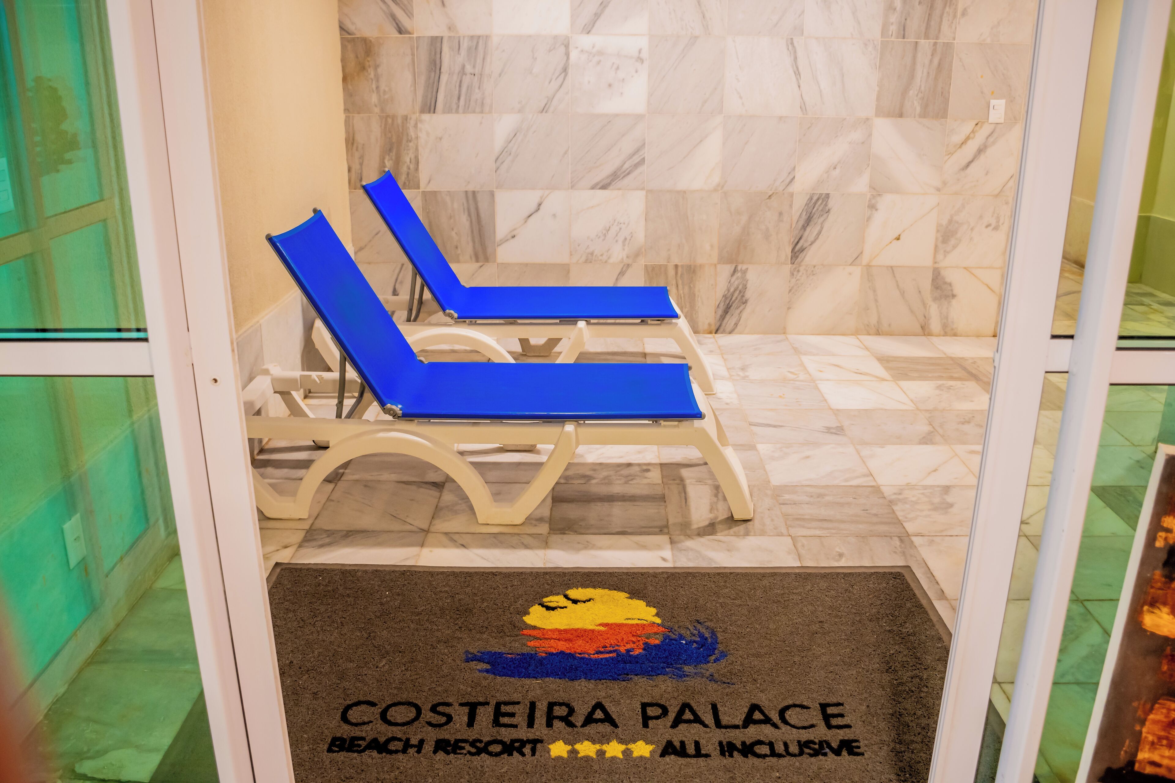 Entrada de um resort à beira-mar, com piso de azulejos e duas espreguiçadeiras azuis.