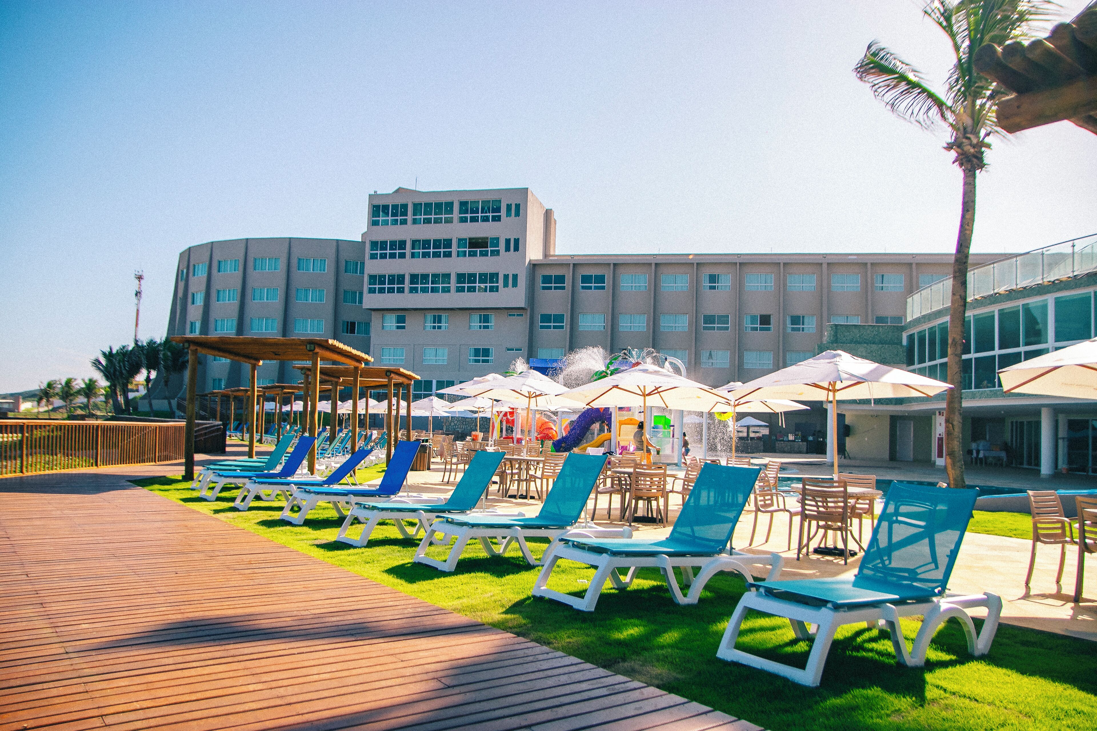 A poolside area with lounge chairs and umbrellas, a wooden deck, and a building in the background.