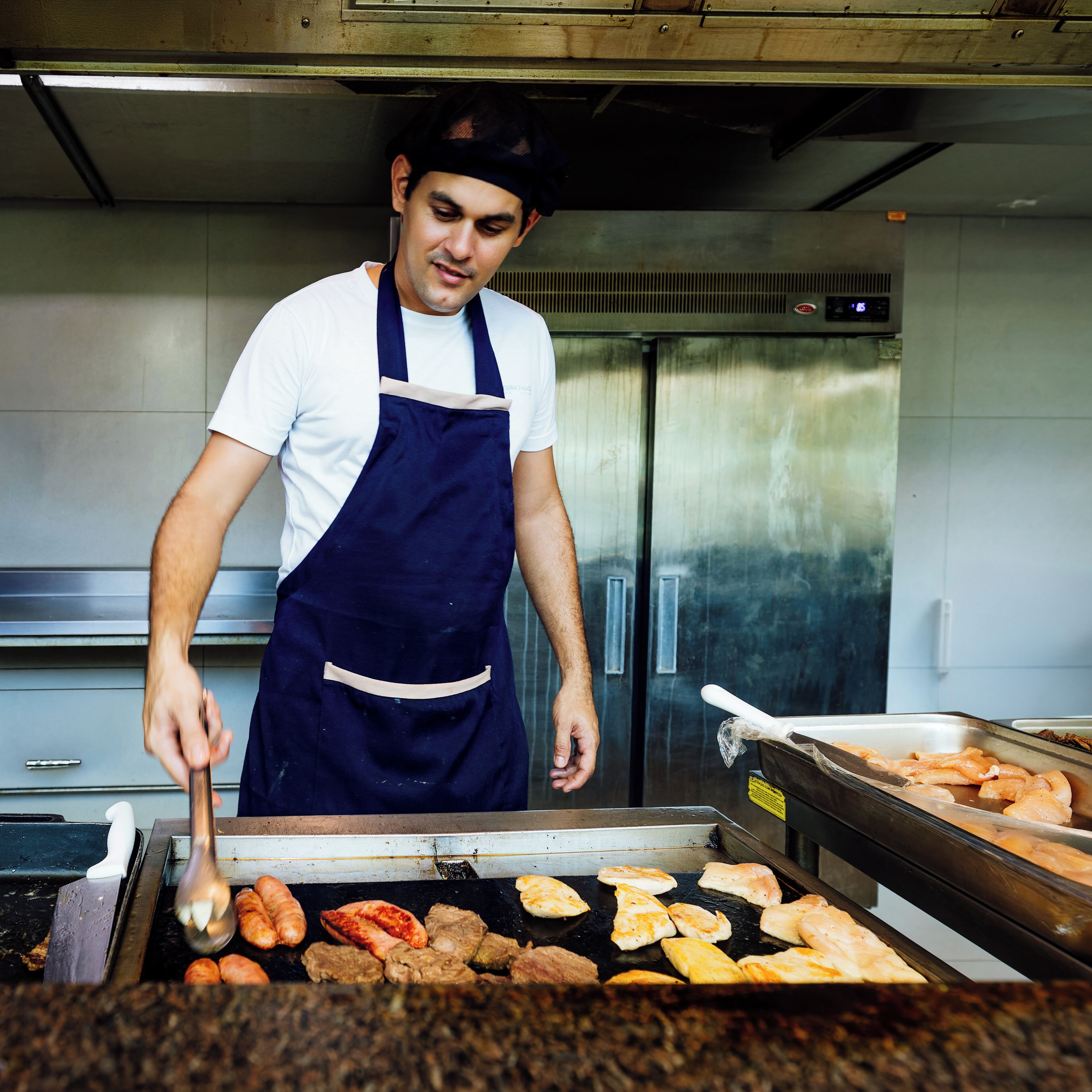 Una persona asando diferentes carnes en una cocina industrial.
