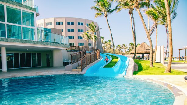 A swimming pool with a blue slide, palm trees, and a building with balconies.