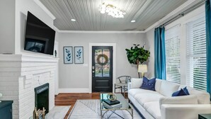 A modern living room with a white fireplace, a sofa, a coffee table, and a large window with blinds. - The Indigo - 2BR w/Hot Tub & Outdoor Space (Columbia)