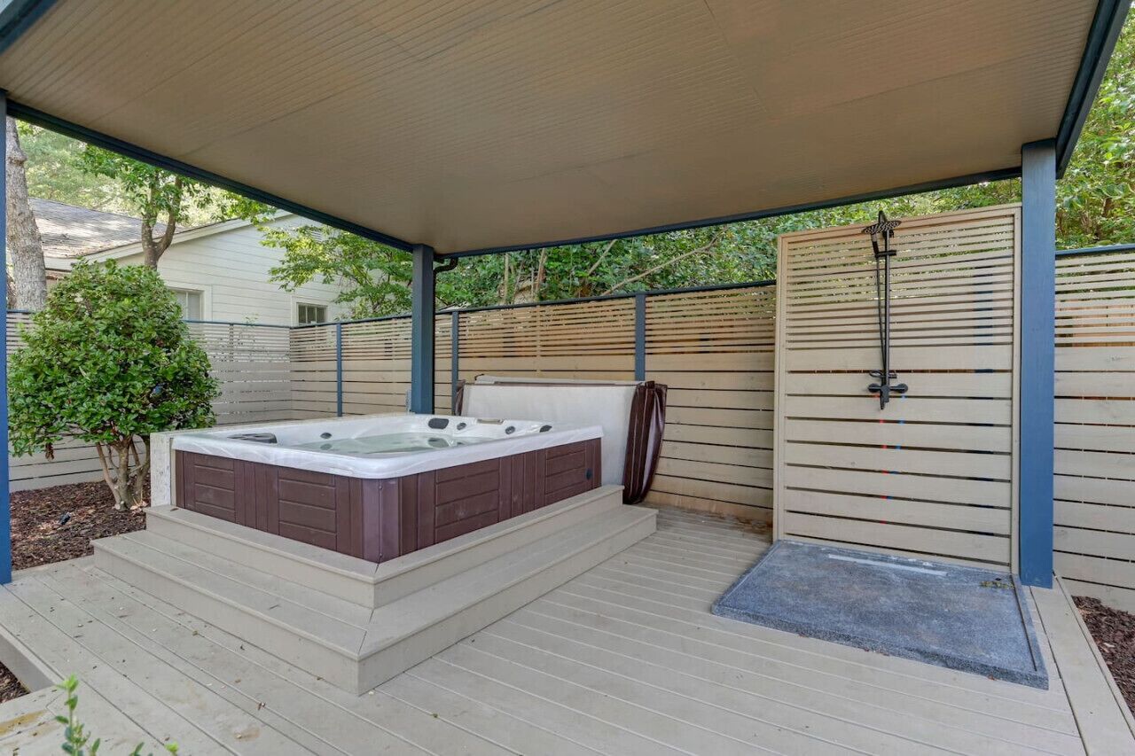 A covered outdoor hot tub area with steps leading up to it, surrounded by a wooden fence and a metal gate.