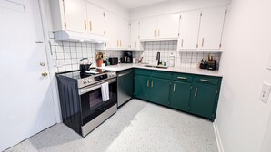 Una cocina con armarios blancos, una estufa negra y muebles bajos color turquesa.