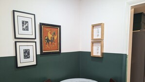 Una habitación de esquina con una mesa redonda y sillas, obras de arte enmarcadas en las paredes, y una decoración en tonos verde y blanco.