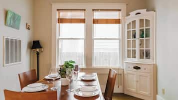 A dining room with a wooden table set for four, two windows with blinds, a white cabinet with glass doors, and a floor lamp.