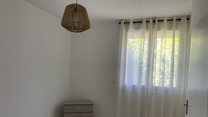Makuuhuoneessa on sänky, puinen lipasto, riippuvalaisin ja ikkuna, jossa on läpikuultavat verhot.