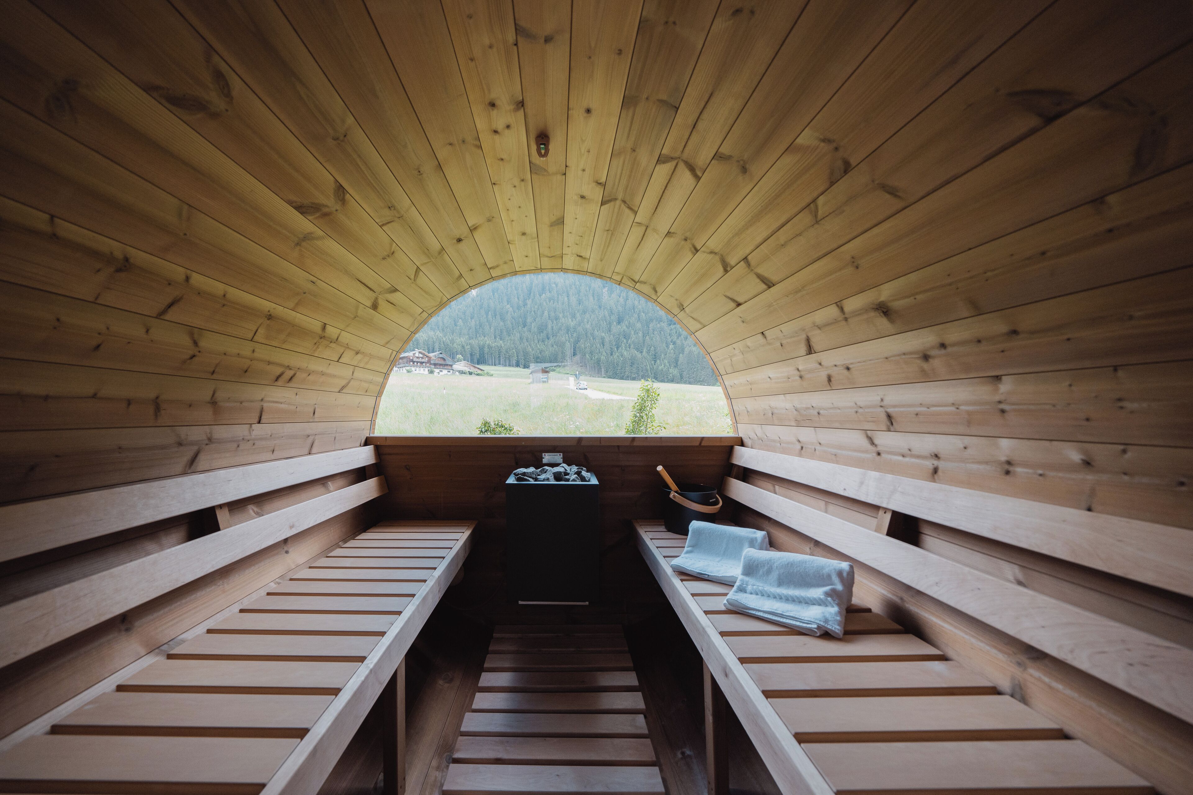 A wooden sauna with benches and a view of a forested area.