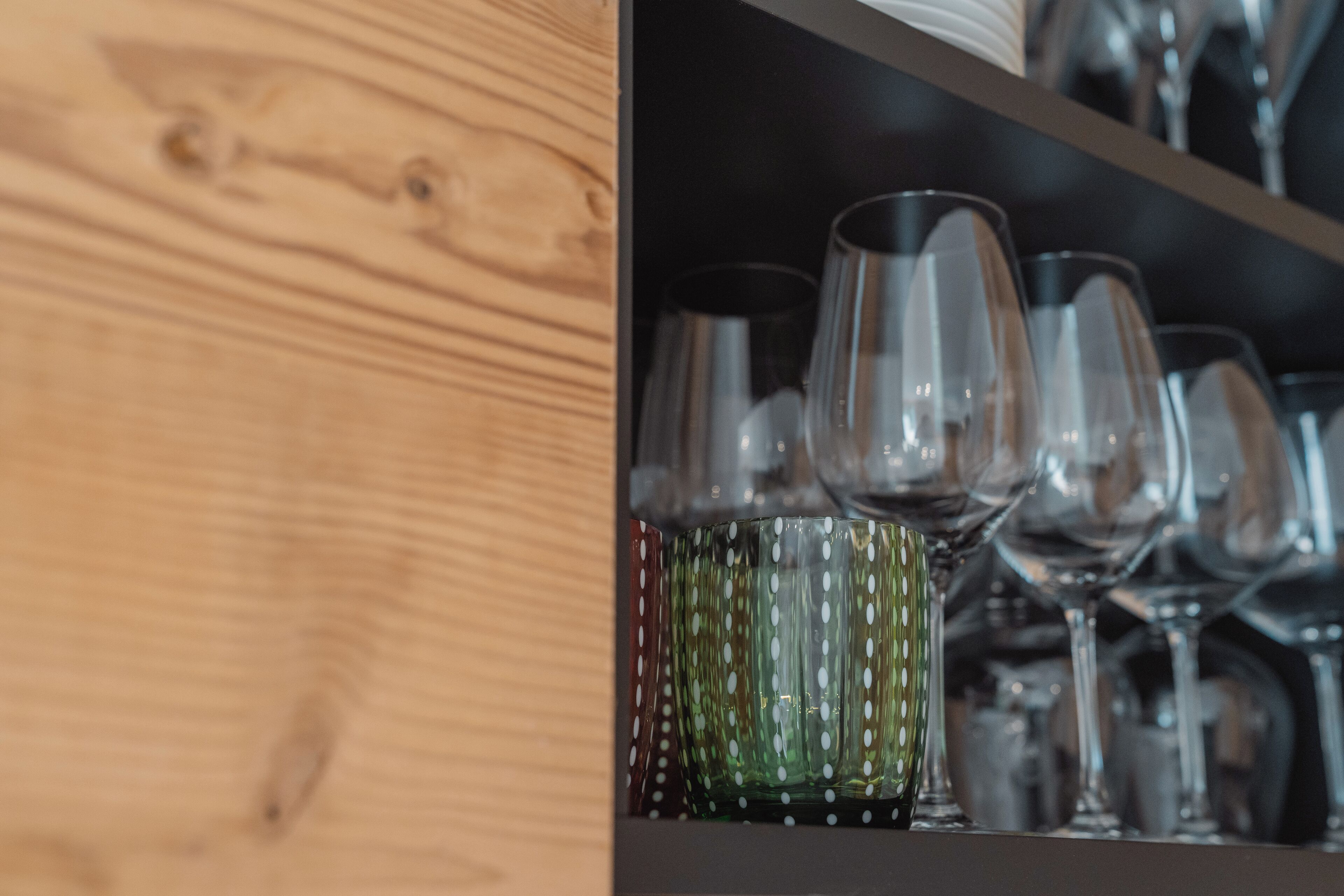 A wooden shelf with various glassware, including wine glasses and a polka-dotted glass.