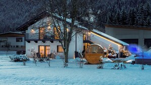A modern house with a wooden deck, a large wooden barrel, and a snow-covered garden.