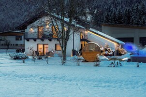 Uma casa moderna com deck de madeira, um grande barril de madeira e um jardim coberto de neve.