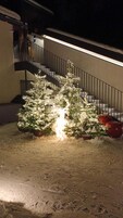 Árvore de Natal coberta de neve, iluminada, em frente a uma escadaria.